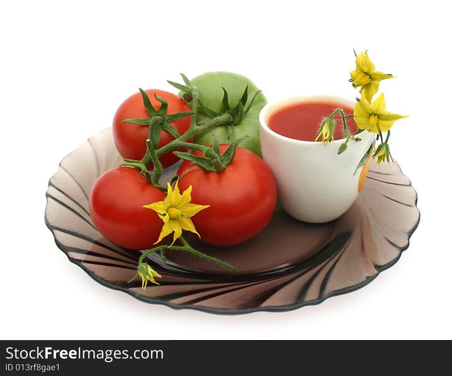 Red tomatoes on a black plate with a white cup of tomato juice on a white background. Red tomatoes on a black plate with a white cup of tomato juice on a white background