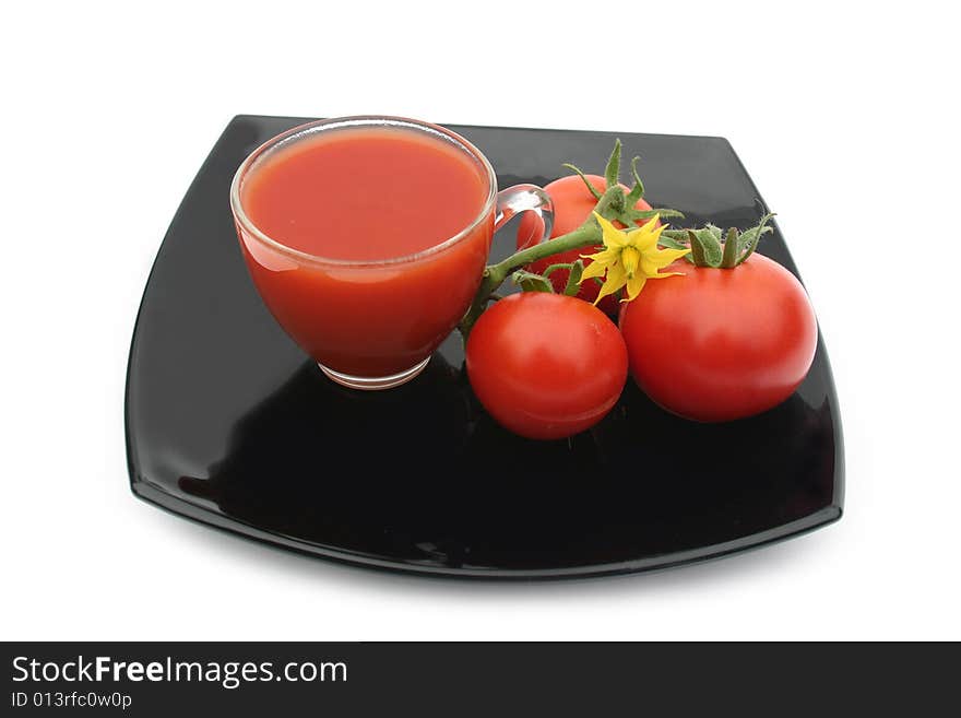 White background and black plate with red tomatoes and a yellow flower