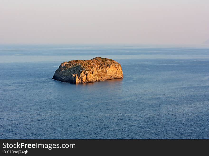 An impressive rock, glowing orange during the sunset, protruding out of the calm sea near Monemvasia, Greece. An impressive rock, glowing orange during the sunset, protruding out of the calm sea near Monemvasia, Greece