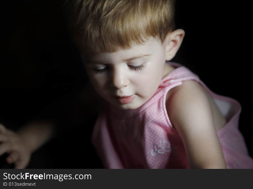 Baby girl with light on a side of her face and in dark on the other is looking down. Baby girl with light on a side of her face and in dark on the other is looking down