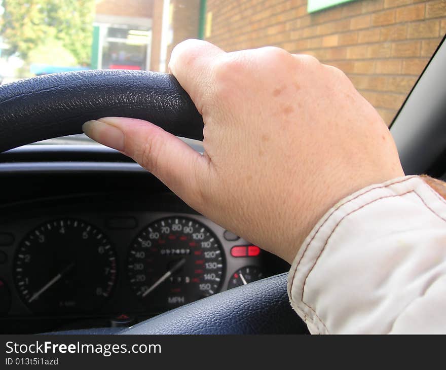 Hand on a steering wheel of a car as the person drives along the road. Hand on a steering wheel of a car as the person drives along the road