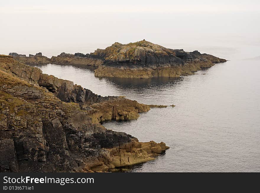 Weatered rocks showing tidal zone markings stretching in a calm sea with  a horizon lost in the mist. Weatered rocks showing tidal zone markings stretching in a calm sea with  a horizon lost in the mist