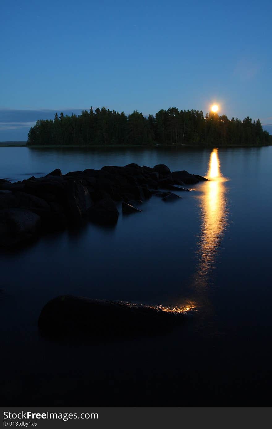 Moon rising and reflecting in the still water of a lake