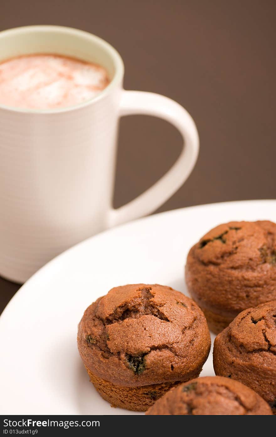 Freshly baked muffins on a white serving plate and hot chocolate in a white cup. Freshly baked muffins on a white serving plate and hot chocolate in a white cup