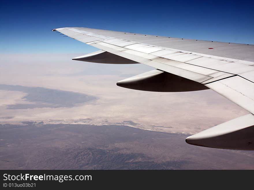 Airplane wing in sky over mountain on a clear day.