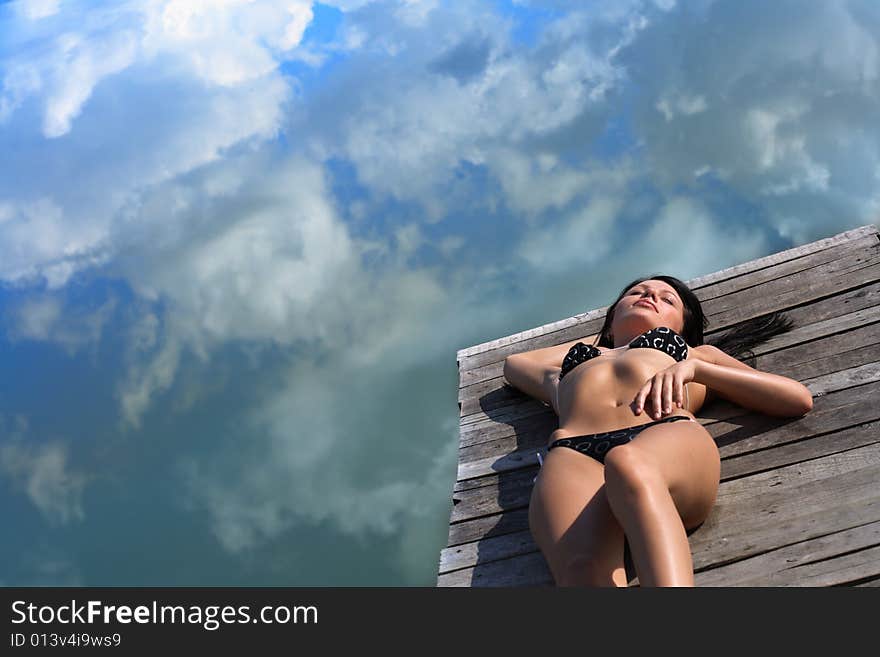 Relaxing woman is lying on a bridge at the water where the blue sky is mirrored. Relaxing woman is lying on a bridge at the water where the blue sky is mirrored