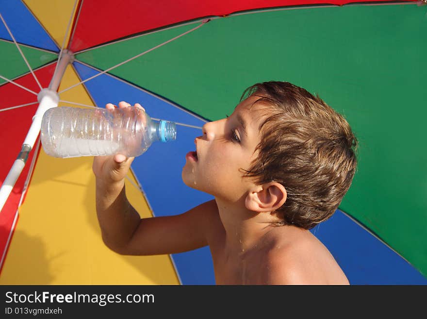 Boy drinking water under the colorful parasol. Boy drinking water under the colorful parasol