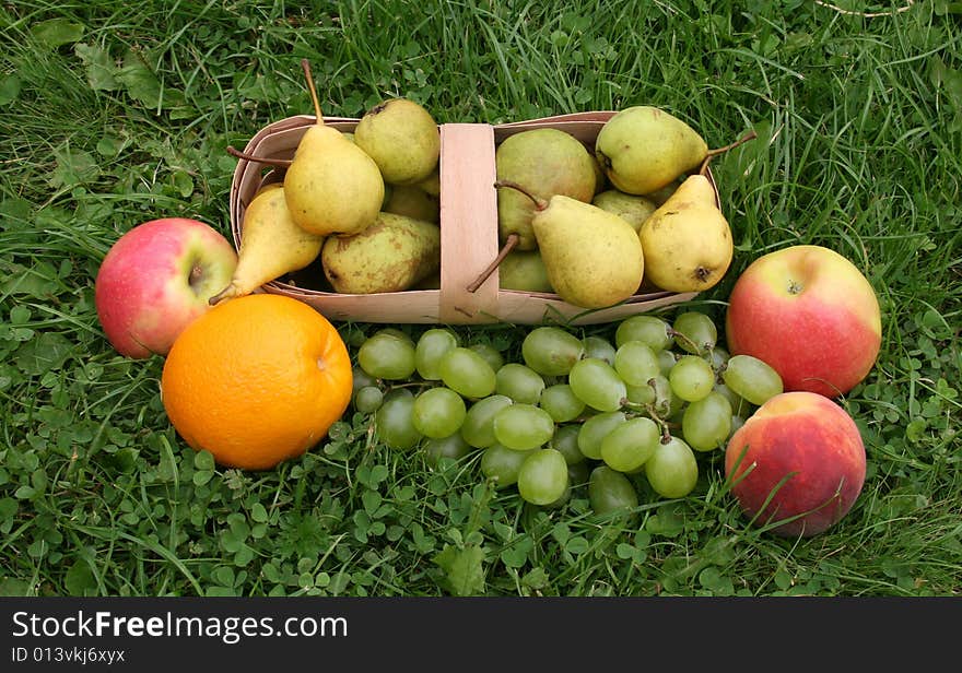 Pears and apples with a peach on a green grass in a basket