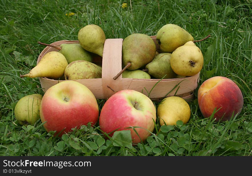 Pears and apples with a 
peach on a green grass in a basket