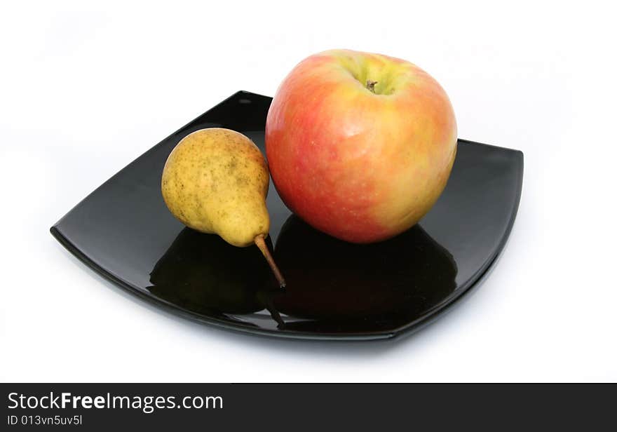 Yellow pear and a ripe apple on a black plate on a 
white background. Yellow pear and a ripe apple on a black plate on a 
white background