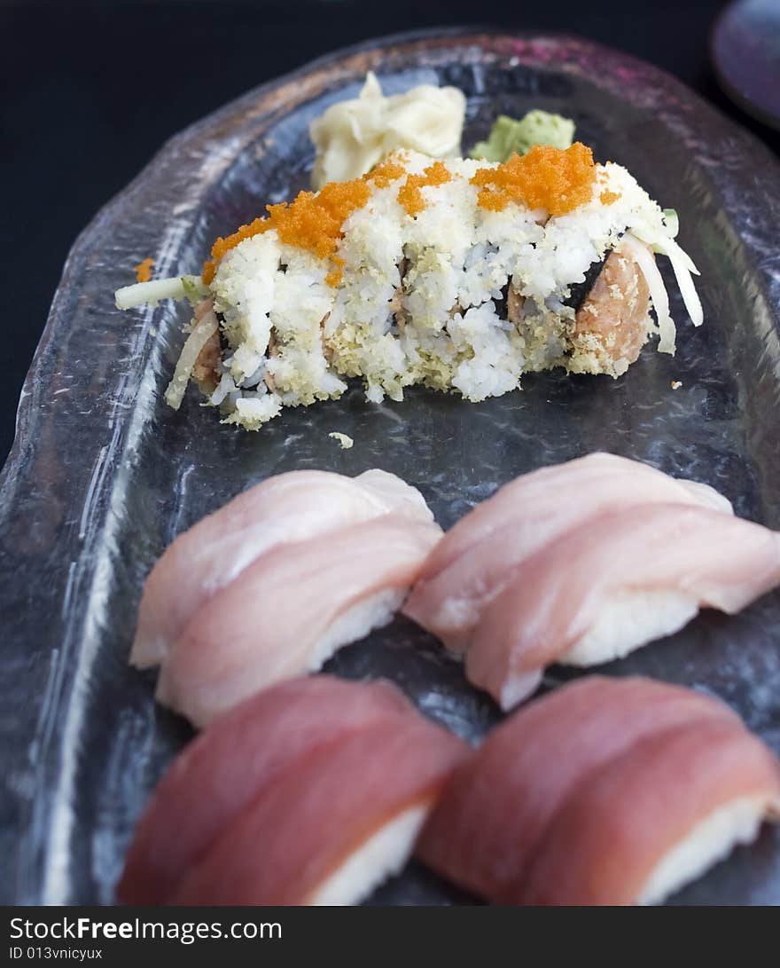 Spicy tuna roll (maki) with flying fish roe (tobiko) garnish on glass serving dish with tuna and yellowtail nigiri sushi. Spicy tuna roll (maki) with flying fish roe (tobiko) garnish on glass serving dish with tuna and yellowtail nigiri sushi