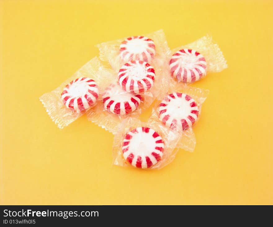 Red and white peppermints in plastic wrappers over yellow background