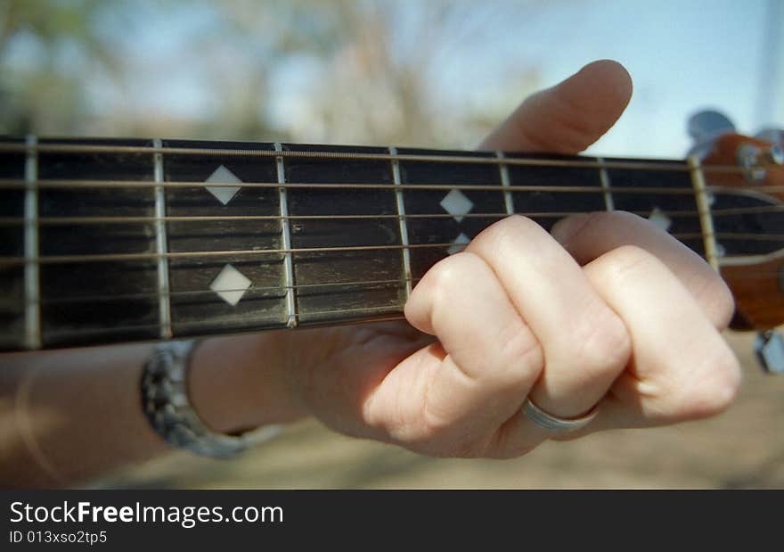 Fingers playing a chord on an acoustic guitar with sunshine. Fingers playing a chord on an acoustic guitar with sunshine