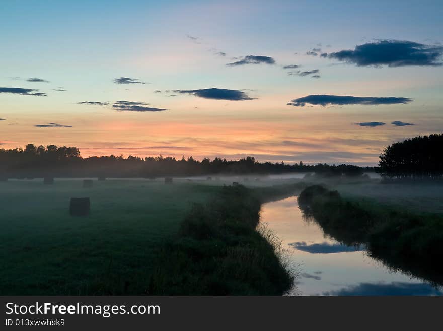 A recently baled farmer's field separated by a creek stands silently at sunset as the mist rises. A recently baled farmer's field separated by a creek stands silently at sunset as the mist rises.