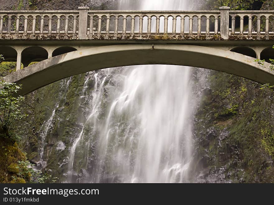 Arched bridge with cascading waterall against mountain rocks. Arched bridge with cascading waterall against mountain rocks