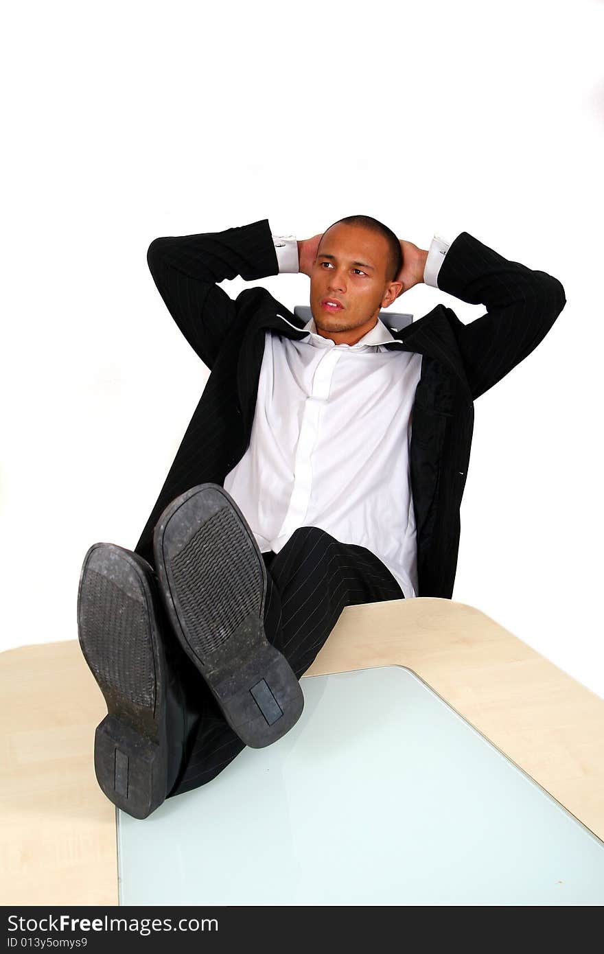 A young satisfied businessman sitting by desk at office feet on table thinking. Isolated over white. A young satisfied businessman sitting by desk at office feet on table thinking. Isolated over white.