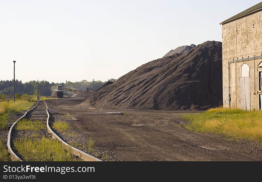 Coal loading in a rail yard on an old train next to massive stacks of coal. Coal loading in a rail yard on an old train next to massive stacks of coal.