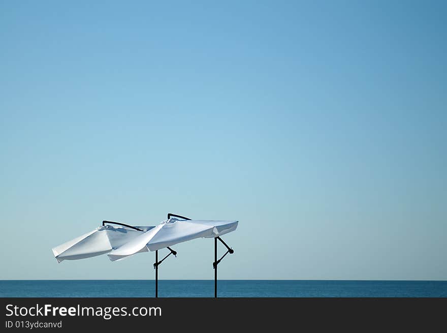 Two lonely white umbrellas over boundless sea open space. Two lonely white umbrellas over boundless sea open space