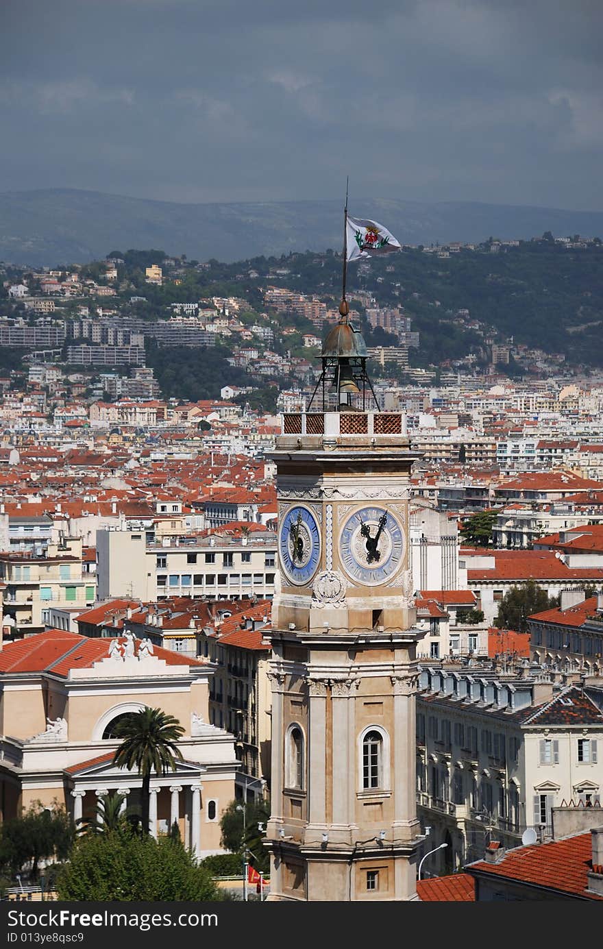 Red tile roofs in old districts, tower of town council with flag in the foreground, dark green hills and grey sky behind, view from above. Red tile roofs in old districts, tower of town council with flag in the foreground, dark green hills and grey sky behind, view from above