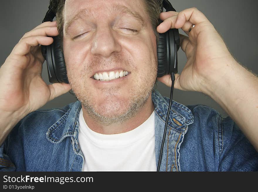 Man with Eyes Shut Wearing Headphones Enjoying His Music on a Grey Background. Man with Eyes Shut Wearing Headphones Enjoying His Music on a Grey Background.