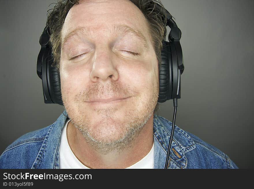 Man with Eyes Shut Wearing Headphones Enjoying His Music on a Grey Background. Man with Eyes Shut Wearing Headphones Enjoying His Music on a Grey Background.