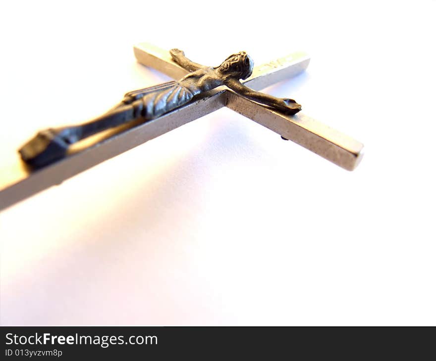 Close shot of a metal crucifix on a white background with a slight shadow. Close shot of a metal crucifix on a white background with a slight shadow.