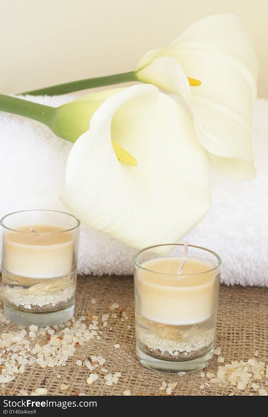 Relaxing spa scene with a white rolled up towel, white lillies, beautiful handmade candles and bath salts