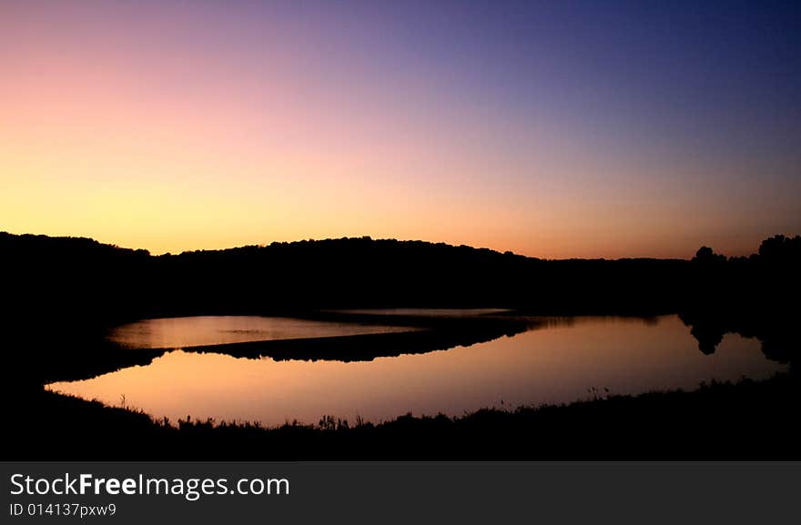 Sunset behind the bluffs over the lake makes beautiful reflections disturbed only by a slight breeze over the water. Sunset behind the bluffs over the lake makes beautiful reflections disturbed only by a slight breeze over the water.