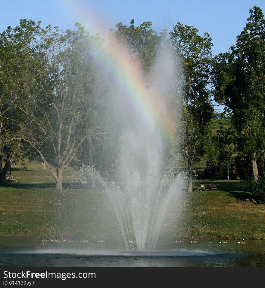 Prism effect of sunlight on fountain mist.  Canadian geese swimming by. Prism effect of sunlight on fountain mist.  Canadian geese swimming by.