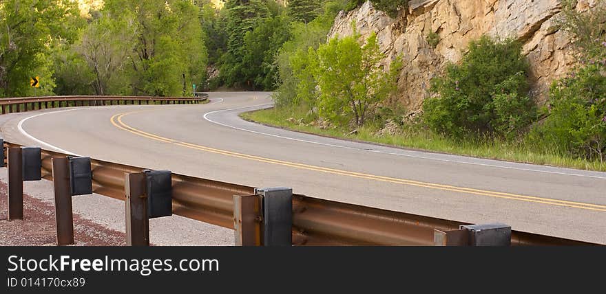 An image of a curving road surrounded by mountains and foliage. An image of a curving road surrounded by mountains and foliage