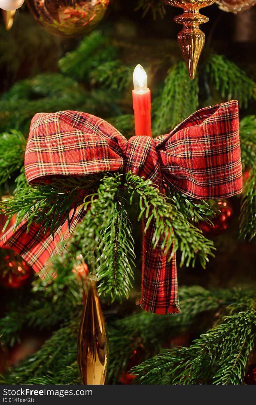 Part of a decorated christmas tree with candle and checkered ribbon