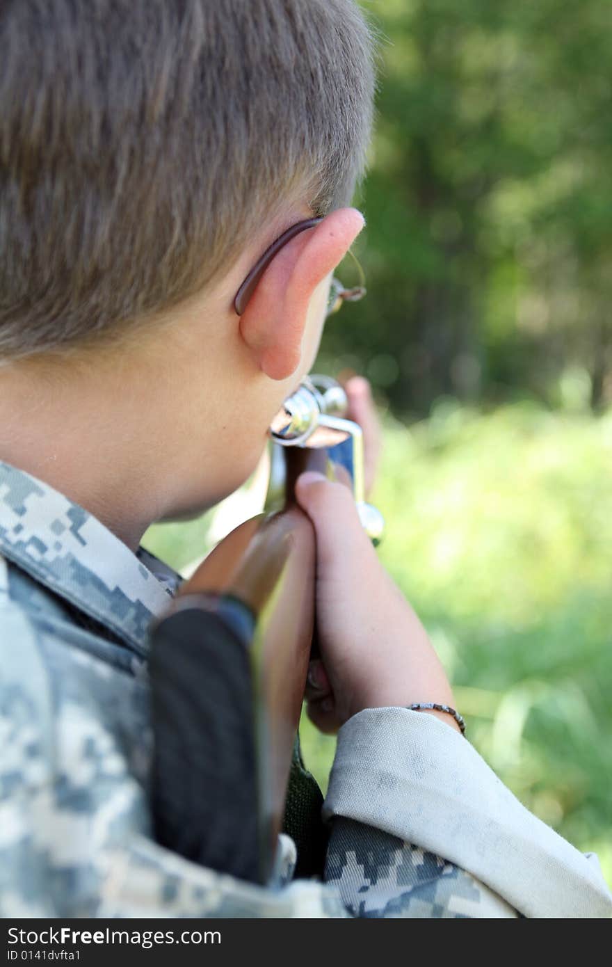 Young child in us army style cammo holding play rifle and aiming it into the woods; child in focus; background intentionally blurred. Young child in us army style cammo holding play rifle and aiming it into the woods; child in focus; background intentionally blurred