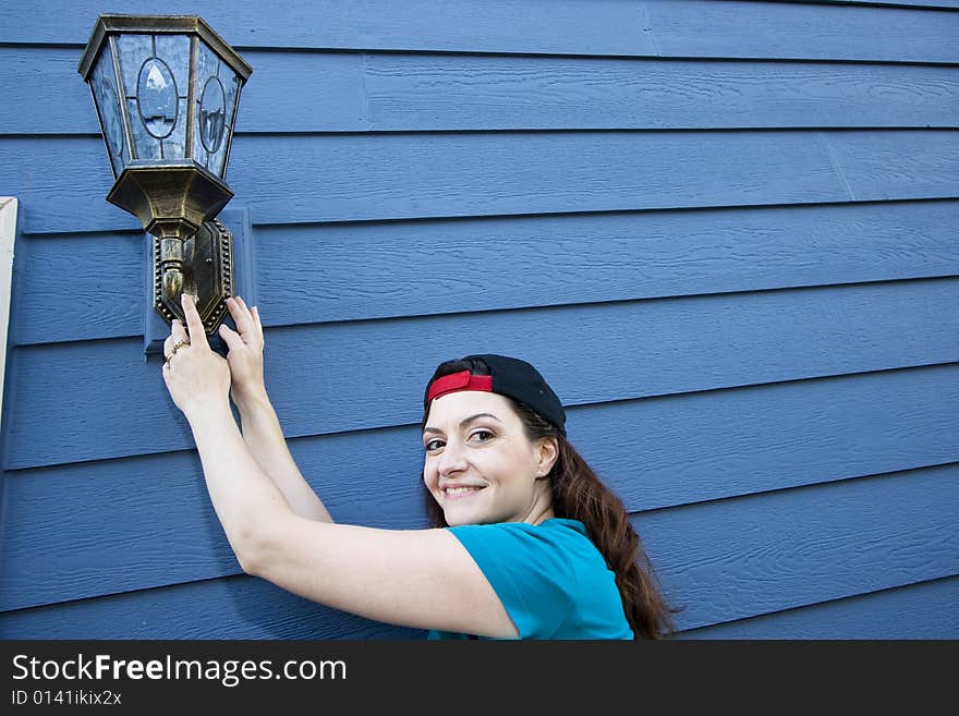 Smiling woman hanging a light fixture on a house. Horizontally framed photo. Smiling woman hanging a light fixture on a house. Horizontally framed photo.