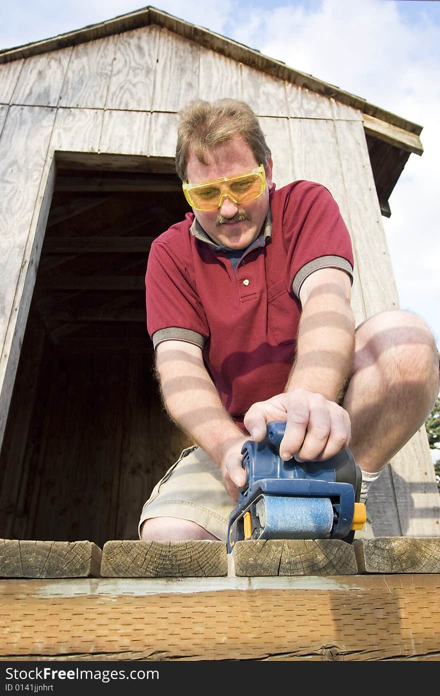 Man wearing safety glasses uses a power sander on wood. Vertically framed photo. Man wearing safety glasses uses a power sander on wood. Vertically framed photo.