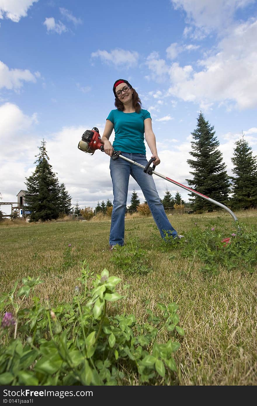 Smiling woman standing in a field using a weedwacker. Vertically framed photo. Smiling woman standing in a field using a weedwacker. Vertically framed photo.