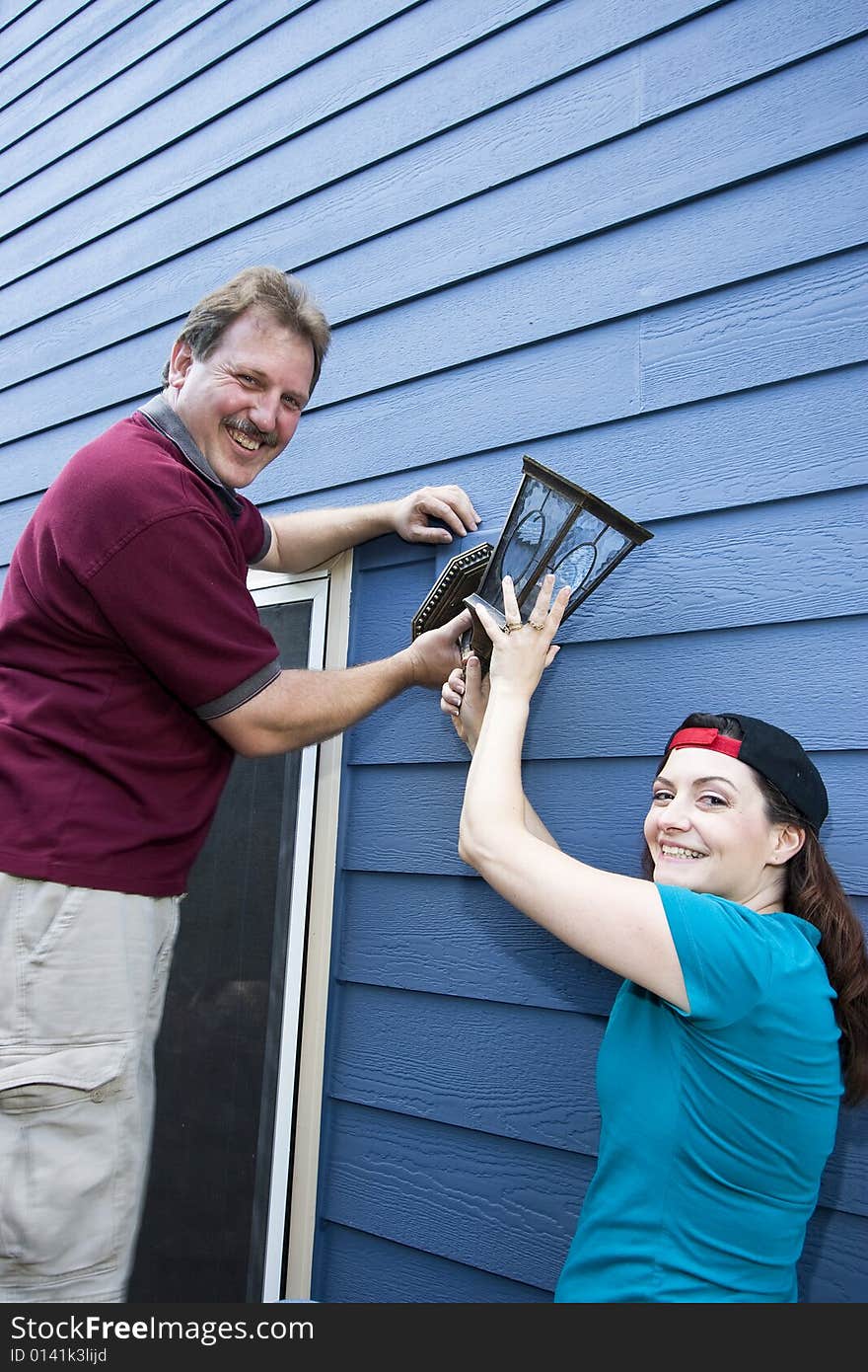 Happy couple hanging a light fixture on a house. Vertically framed photo. Happy couple hanging a light fixture on a house. Vertically framed photo.