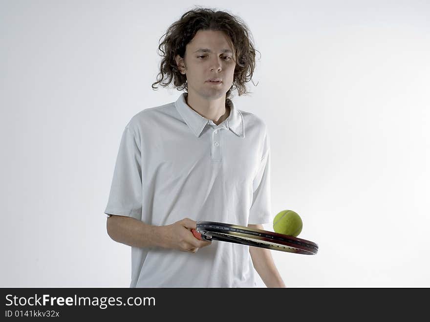 A young man balancing a tennis ball on a racket.  He is focusing on the ball and has a serious expression on his face. Horizontally framed shot. A young man balancing a tennis ball on a racket.  He is focusing on the ball and has a serious expression on his face. Horizontally framed shot.