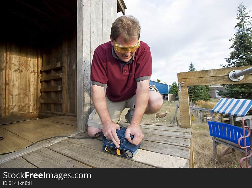 Smiling man with safety glasses using a power sander on some wood. Horizontally framed photo. Smiling man with safety glasses using a power sander on some wood. Horizontally framed photo.