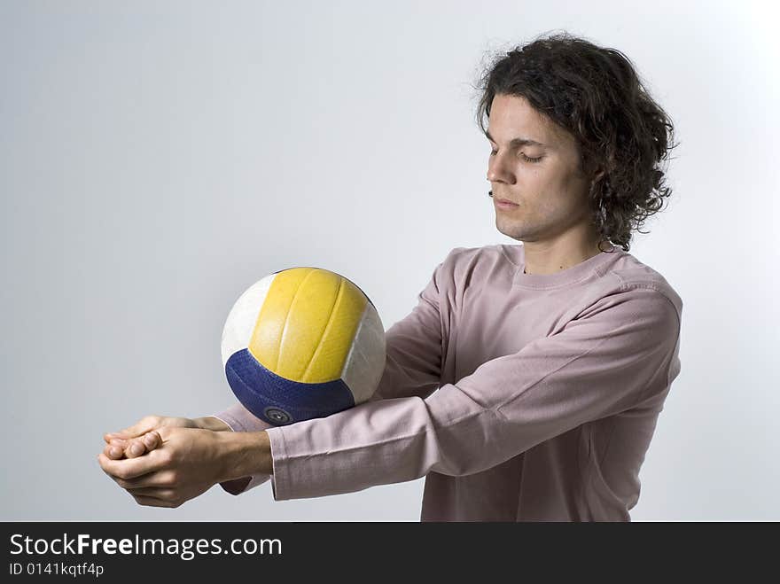 An athlete balancing a volleyball on his forearms. His hands are clasped and his eyes are closed in concentration.  He has a serious expression on his face. Horizontally framed shot. An athlete balancing a volleyball on his forearms. His hands are clasped and his eyes are closed in concentration.  He has a serious expression on his face. Horizontally framed shot.