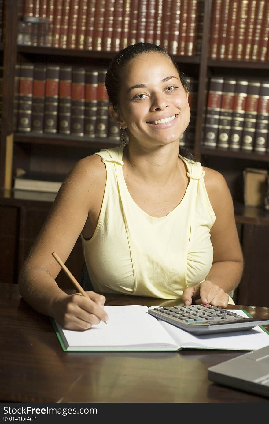 Female student smiling as she sits at a desk writing and using a calculator. Vertically framed photo. Female student smiling as she sits at a desk writing and using a calculator. Vertically framed photo.