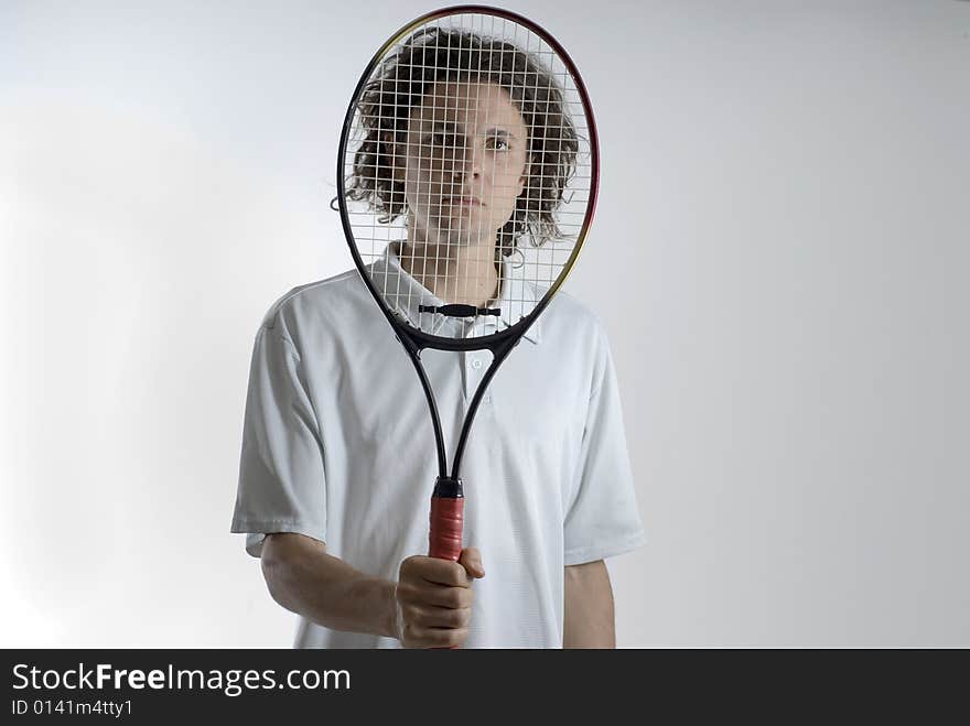 An athlete holding a tennis racket over his face.  He is looking through the racket at the camera.  He has a serious expression on his face. Horizontally framed shot. An athlete holding a tennis racket over his face.  He is looking through the racket at the camera.  He has a serious expression on his face. Horizontally framed shot.