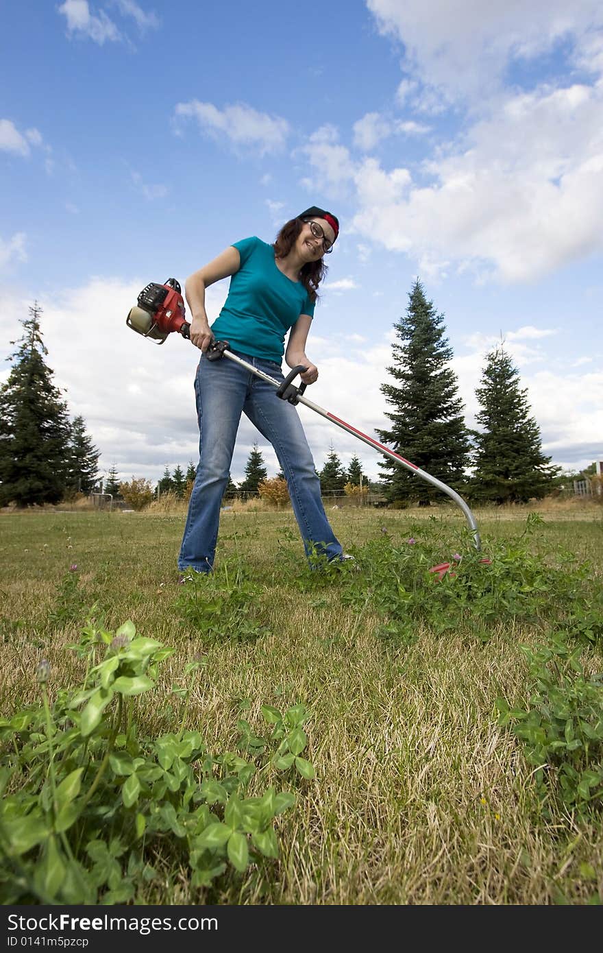 Angry woman standing in a field using a weedwacker. Vertically framed photo. Angry woman standing in a field using a weedwacker. Vertically framed photo.