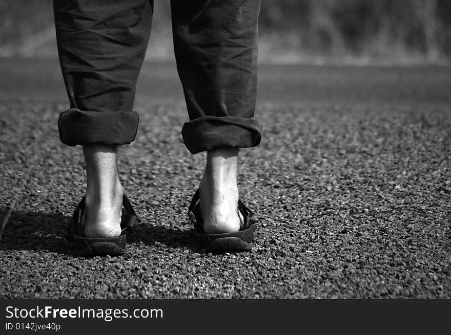 B/W feet with sandals before road. B/W feet with sandals before road