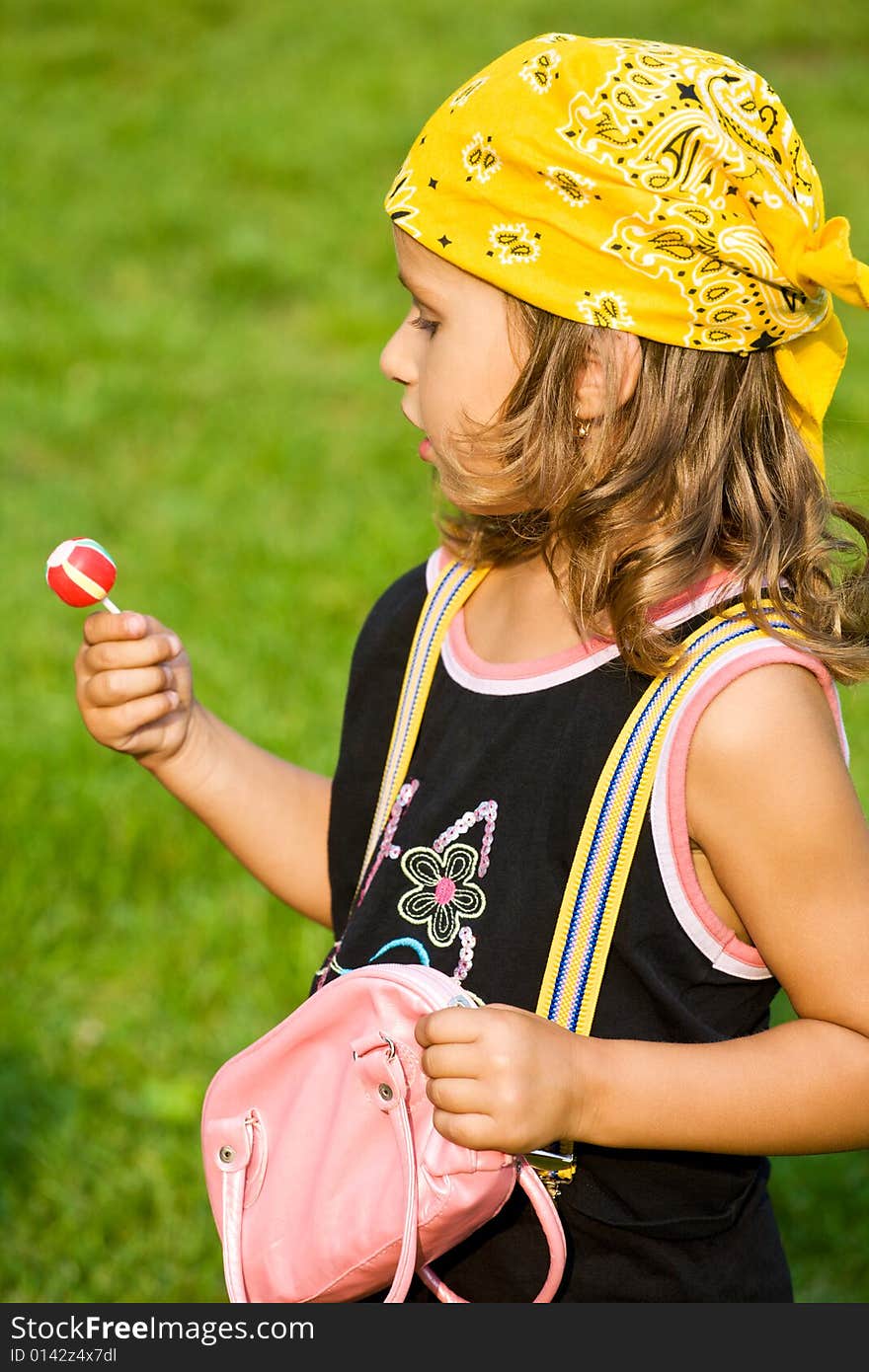 Closeup portrait of little girl with lollipop and bag on green grass. Closeup portrait of little girl with lollipop and bag on green grass