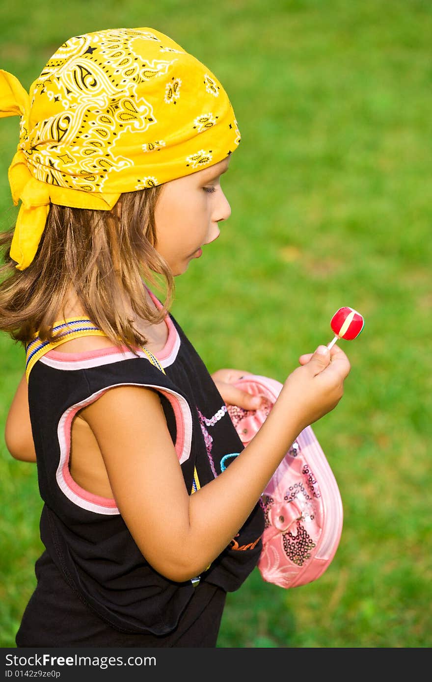 Closeup portrait of little girl with lollipop and bag on green grass. Closeup portrait of little girl with lollipop and bag on green grass