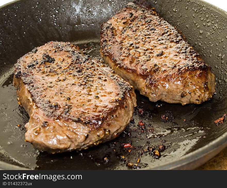 Two beef steaks spiced with black pepper in a saucepan. Two beef steaks spiced with black pepper in a saucepan