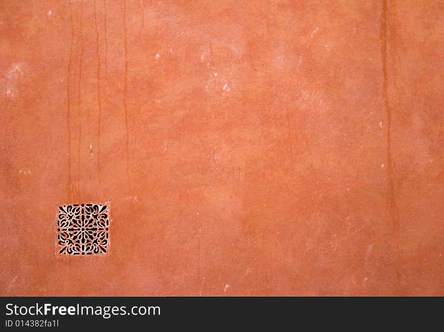 Closeup of red-brown old stucco wall with ornate ventilation grid. Closeup of red-brown old stucco wall with ornate ventilation grid