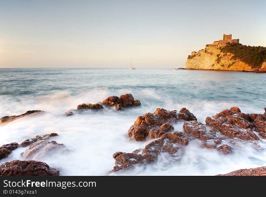 Seaside landscape: sea over rocks, in background the castle of Castiglione, Tuscany, Italy.