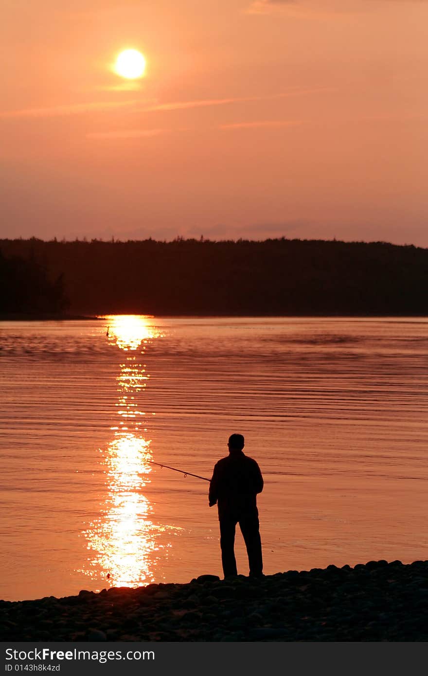 The silhouette of a man fishing at sunset.