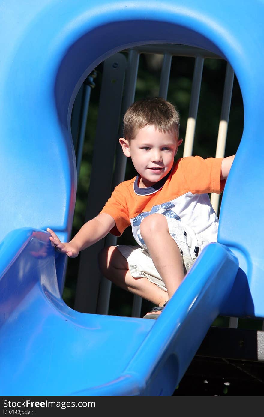Young boy at the top of a shiny blue slide getting ready to go down